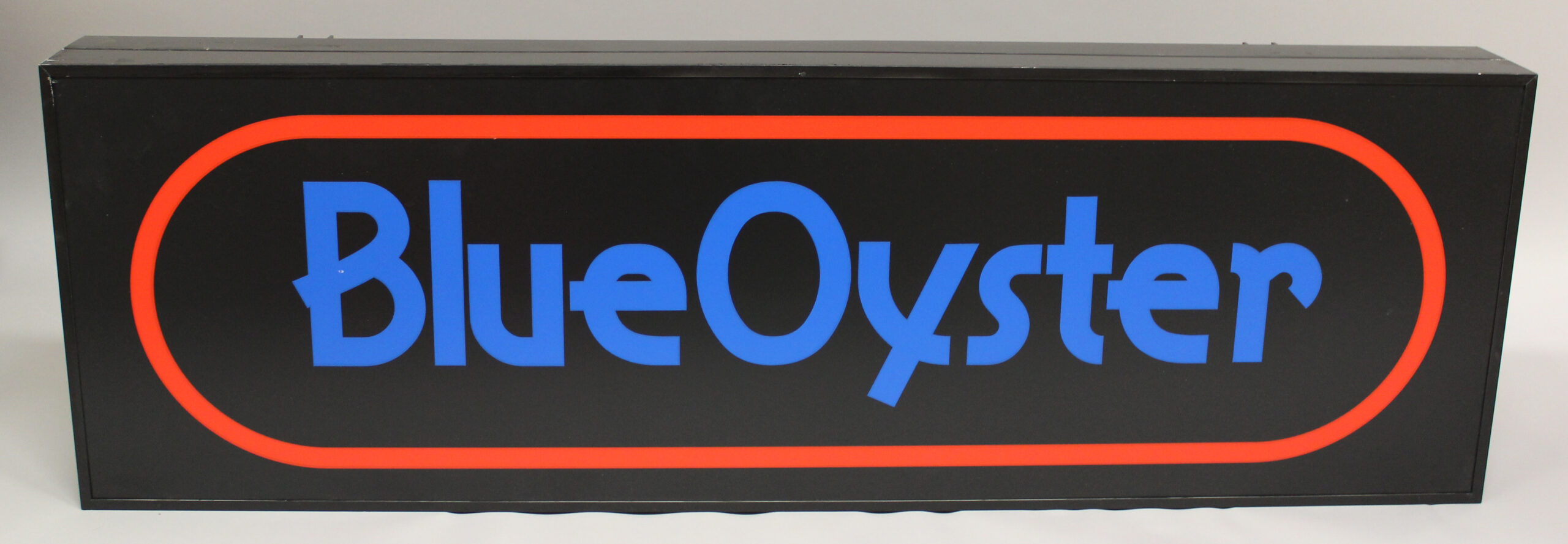 Kuva mustasta valomainoksesta, jossa on punaisen renkaan sisällä teksti Blue Oyster.