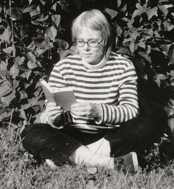 En ung person sitter med benen i kors på gräsmattan och läser en bok.
