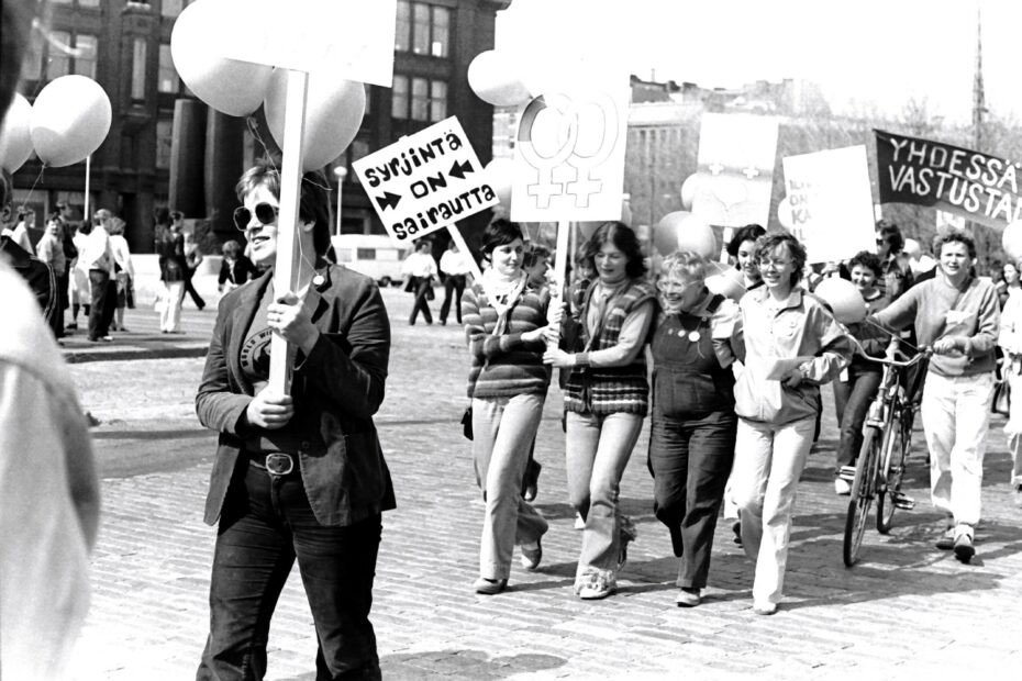 Mieltä osoittavia iloisia naisia. Kyltissä teksti "syrjintä on sairautta".